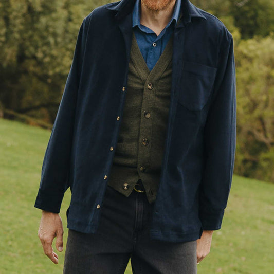Man wearing a navy jacket over a blue shirt with a green vest outdoors.