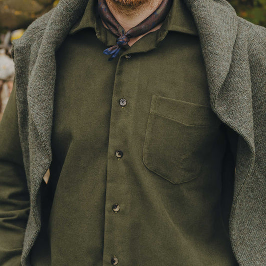 Person wearing a green shirt with a pocket and a green jumper over shoulders.