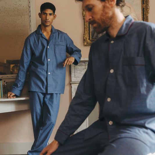 Two men wearing matching blue pyjama sets in a room with a painting on the wall.