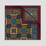 A square silk-like pocket square with a richly patterned design, featuring a deep burgundy border and a central medallion motif in navy blue, gold, and light blue, shown on a neutral gray background.