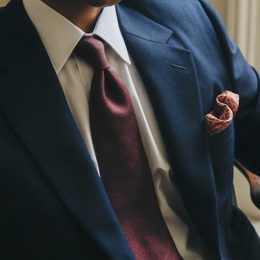 Man wearing a navy suit with a maroon tie and pocket square.