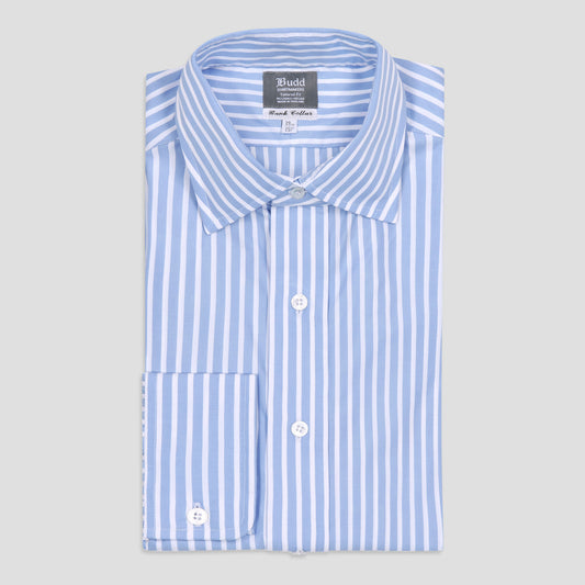 A folded light blue and white vertically striped dress shirt with a pointed collar, white buttons, and a single chest pocket, shown on a light gray background. The brand label reads 'Budd'.