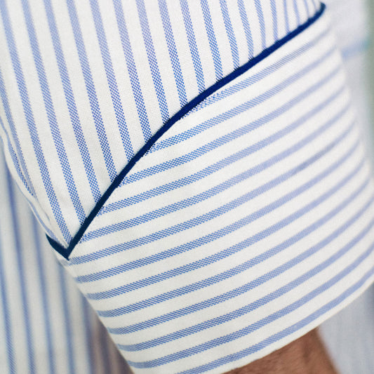 Close-up of a white and blue striped gown, showing a pocket with dark blue piping and part of a person's arm.