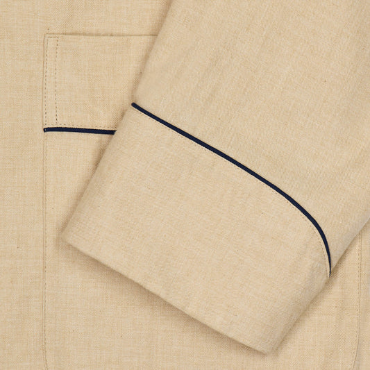 Close-up of a beige linen pajama or shirt fabric with a pocket and dark navy piping detail along the cuff and pocket edge.