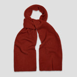 A rust-red ribbed knit scarf, knotted at the top, displayed against a solid light gray background.