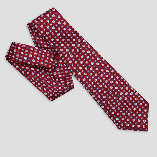 A red necktie with a repeating white and light blue floral pattern, shown on a light gray background.