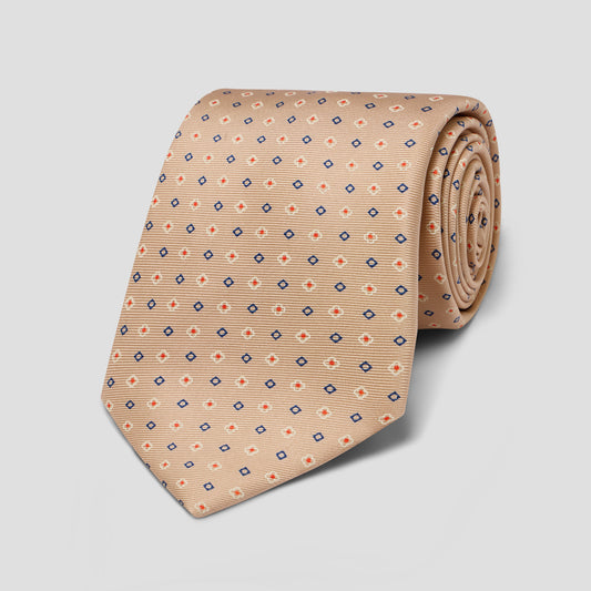 A rolled beige necktie with a repeating geometric pattern of small blue and orange diamond motifs, displayed on a neutral light gray background.