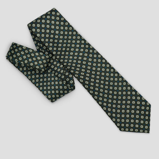 A navy blue necktie with a repeating pattern of small, light cream-colored leaf-like shapes, arranged on a neutral light gray background.