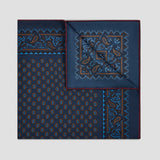 A folded navy blue silk-like pocket square with intricate paisley and geometric patterns in blue, brown, and gold, displayed on a neutral light gray background.