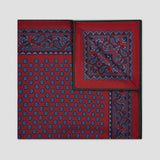 A folded red silk pocket square with a navy blue paisley pattern and repeating anchor motifs, displayed on a light gray background.