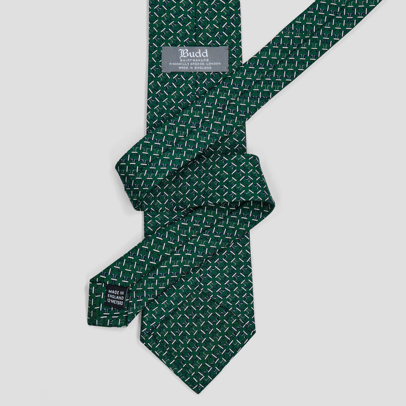 A dark green necktie with a repeating geometric diamond pattern in white and light green, styled in a knot on a light gray background. The brand label reads 'Tebudd'.