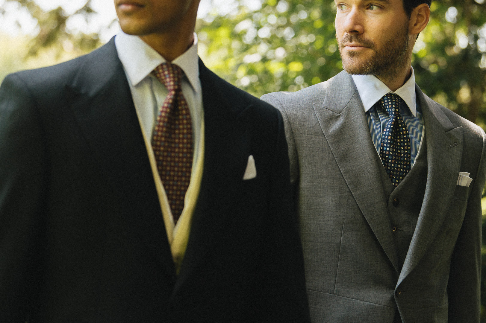 Two men in suits standing outdoors with trees in the background