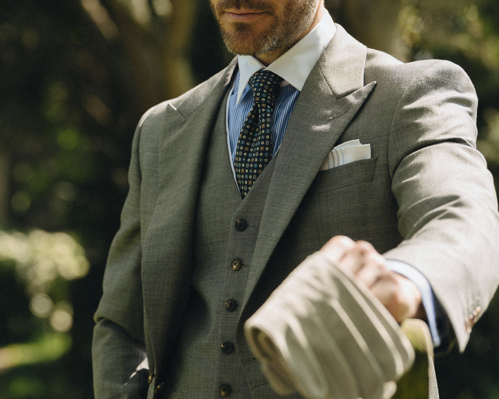 Man in a gray suit holding an umbrella outdoors at wedding