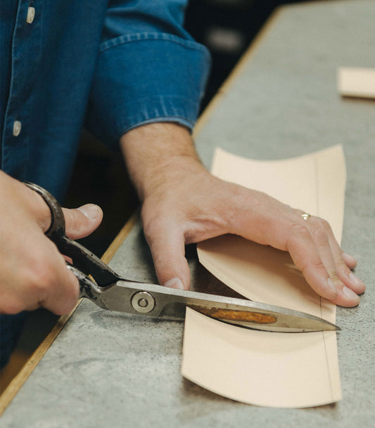 Person cutting a piece of fabric with scissors on a table.