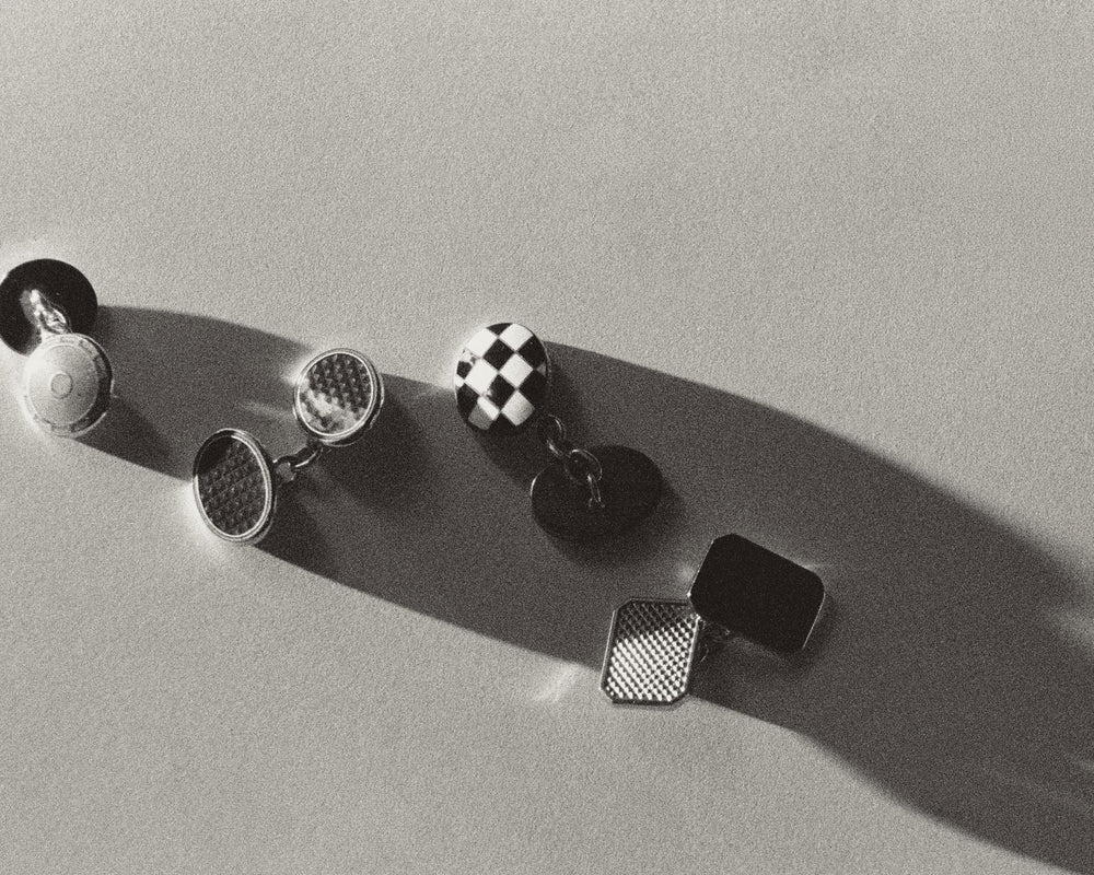 Black tie evening dress wear cufflinks laid out on neutral background with dramatic shadows