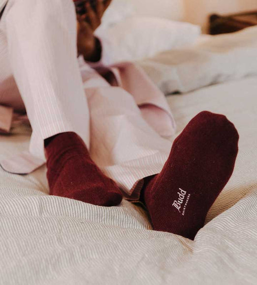 Person wearing burgundy socks with a brand logo on a bed.