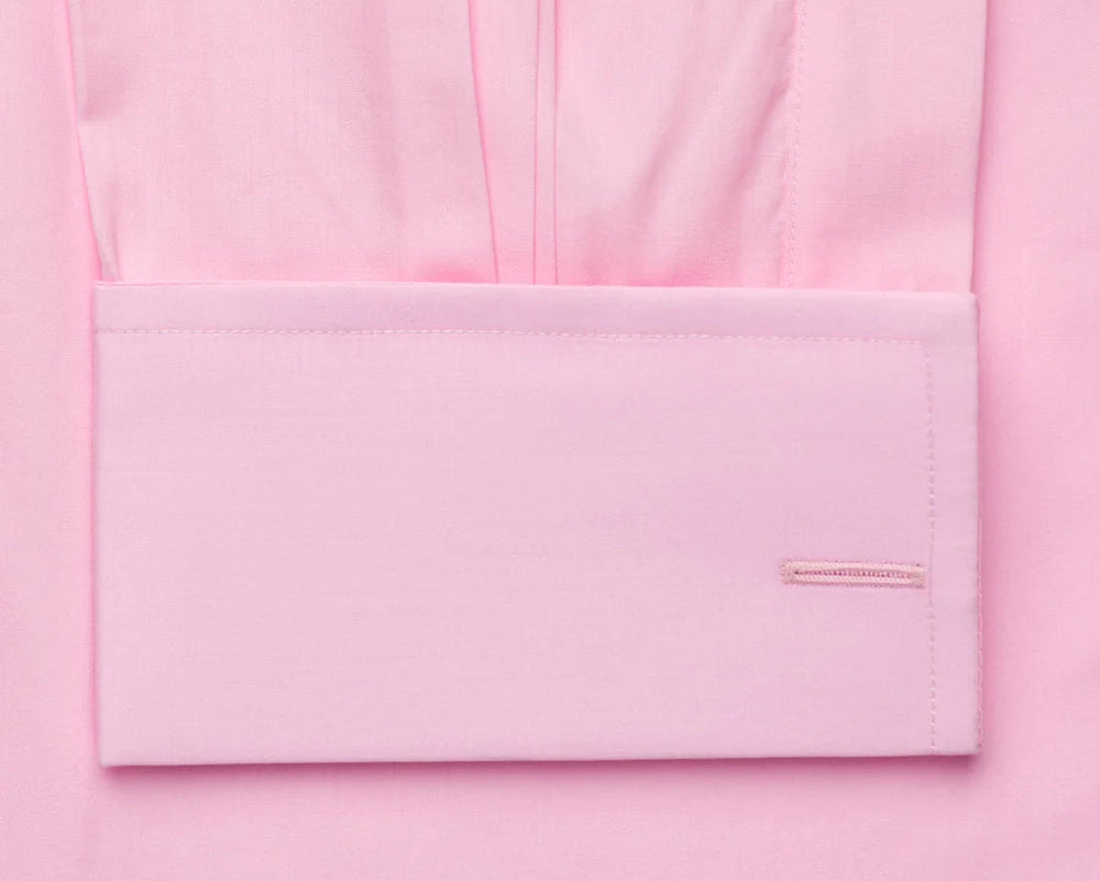 A close-up of a light pink dress shirt showing the front body fabric and a folded cuff with neat stitching and a small tonal brand tab.