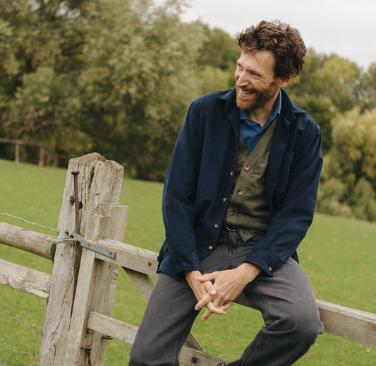 Man sitting on a wooden gate in a green field with trees in the background