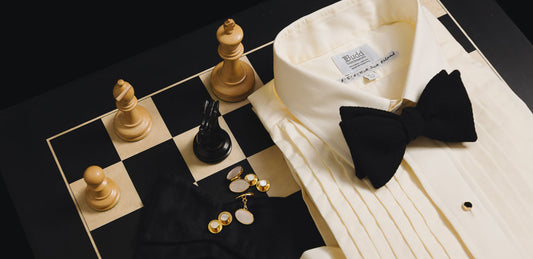 Black tie shirt, bow tie and accessories laid on chess board with chess pieces