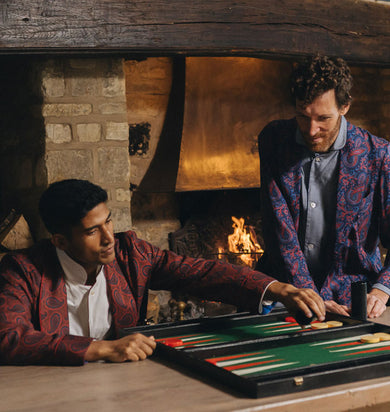 Two men playing backgammon in front of a fireplace