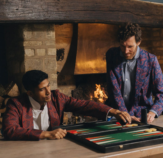 Two men playing backgammon in a cozy room with a fireplace.