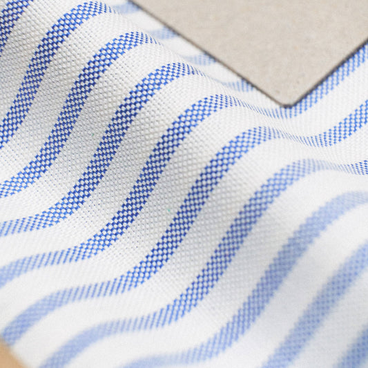 Close-up of a white woven fabric with repeating blue wavy stripes and a plain beige square sample placed on top.