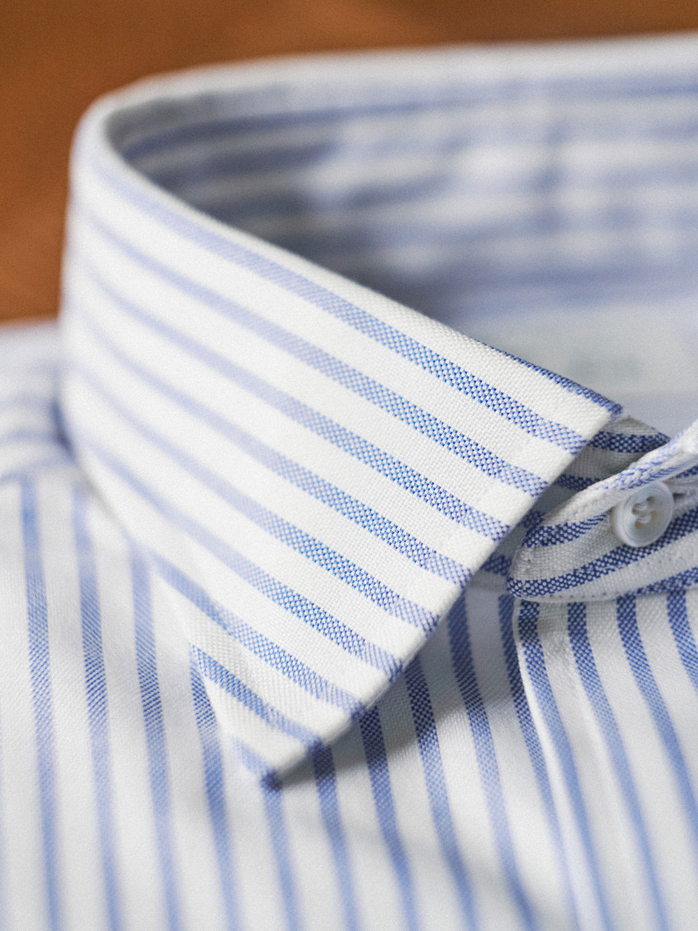 Close-up of a blue and white striped dress shirt collar with a white button, showing the fabric texture and pattern.