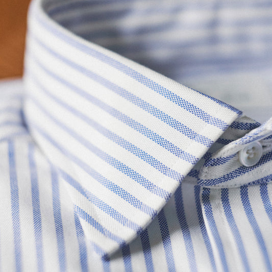 Close-up of a blue and white striped dress shirt collar with a white button, showing the fabric texture and pattern.