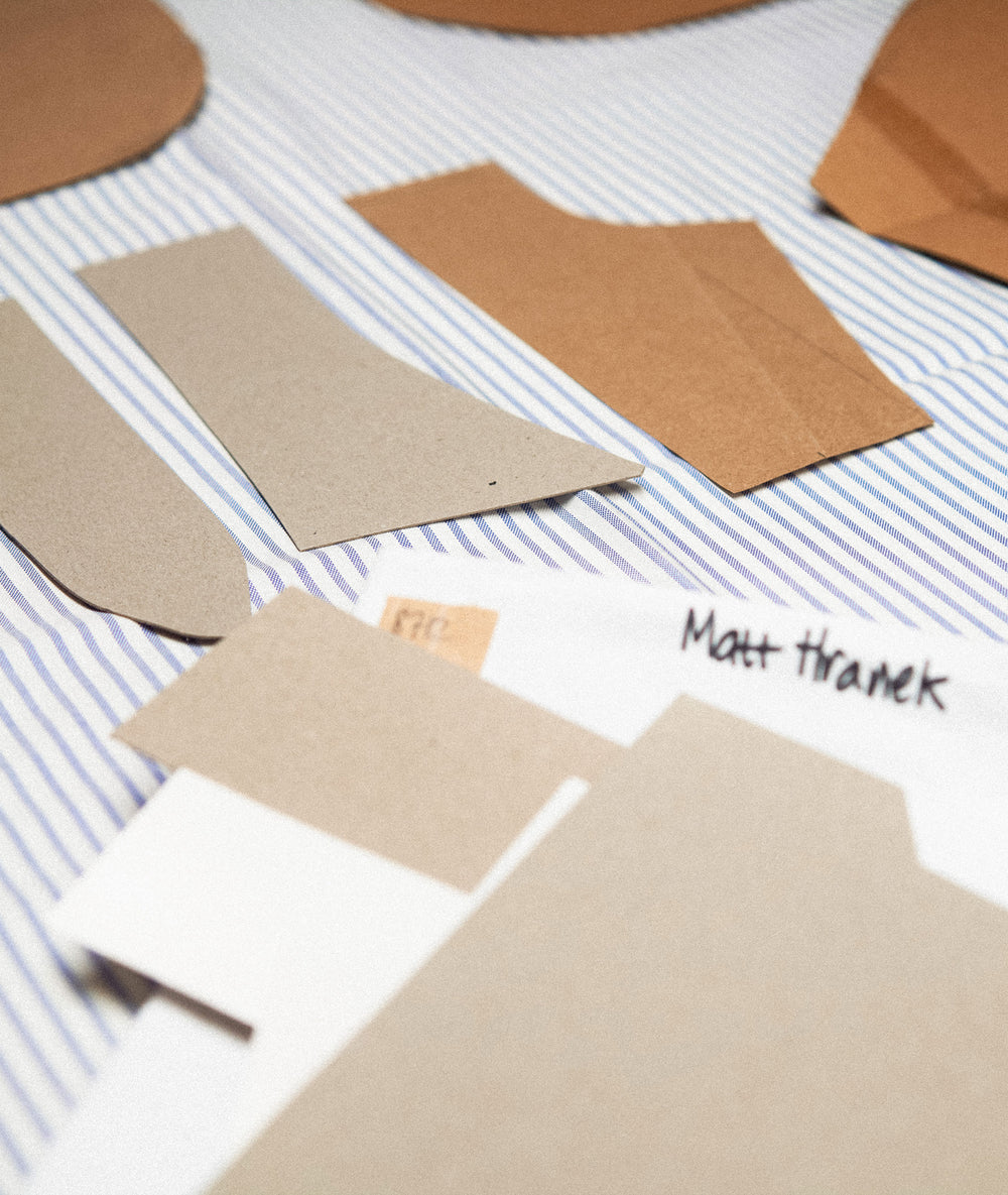 Several brown paper pattern pieces and a white paper template labeled 'Matt Thranek' are arranged on a blue-and-white striped fabric background.