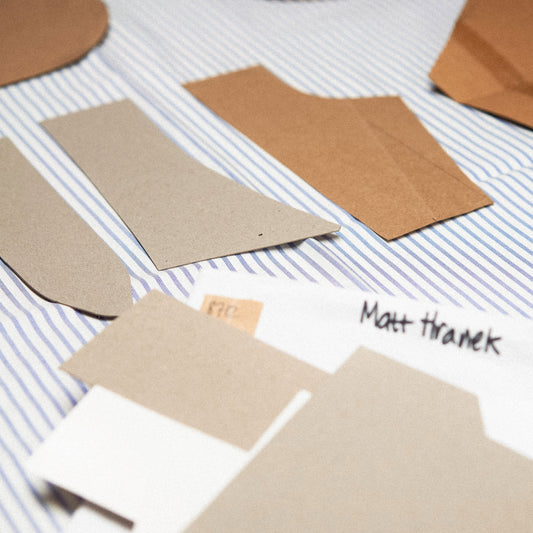 Several brown paper pattern pieces and a white paper template labeled 'Matt Thranek' are arranged on a blue-and-white striped fabric background.