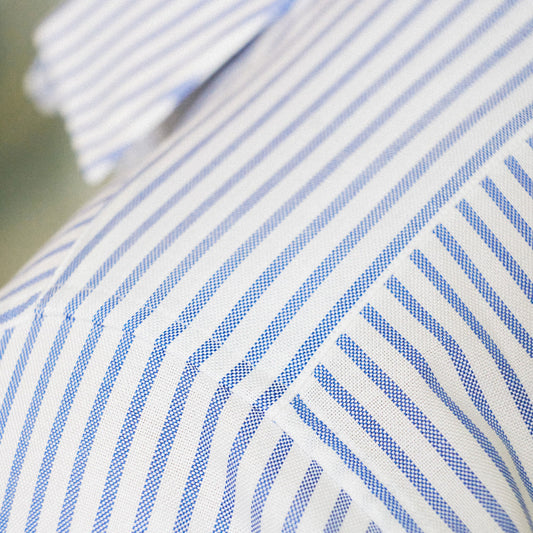 Close-up of a white fabric with thin blue diagonal stripes, showing the texture and collar area.