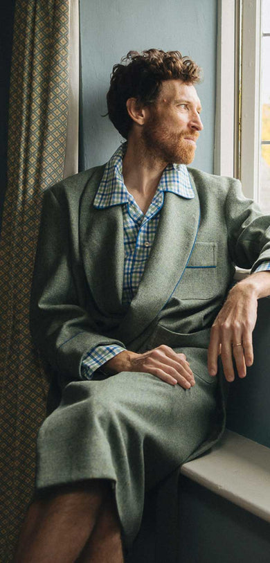 Man sitting by a window wearing a robe, looking out.