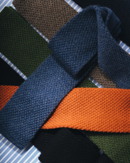 Multi coloured knitted ties laid on blue stripe background