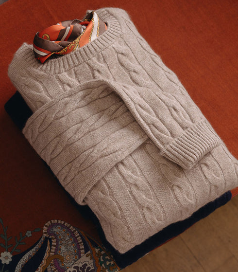 Folder beige cable knit sweater laid on orange cloth