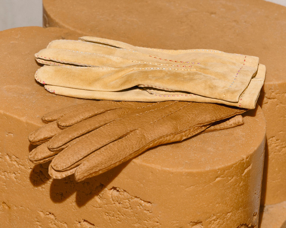 Two leather work gloves, one light tan and one medium brown, displayed on a textured tan stone pedestal.