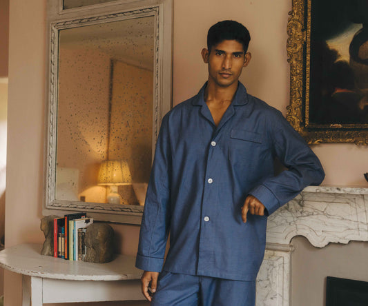 Man wearing blue pyjamas standing in a room with a mirror and painting.