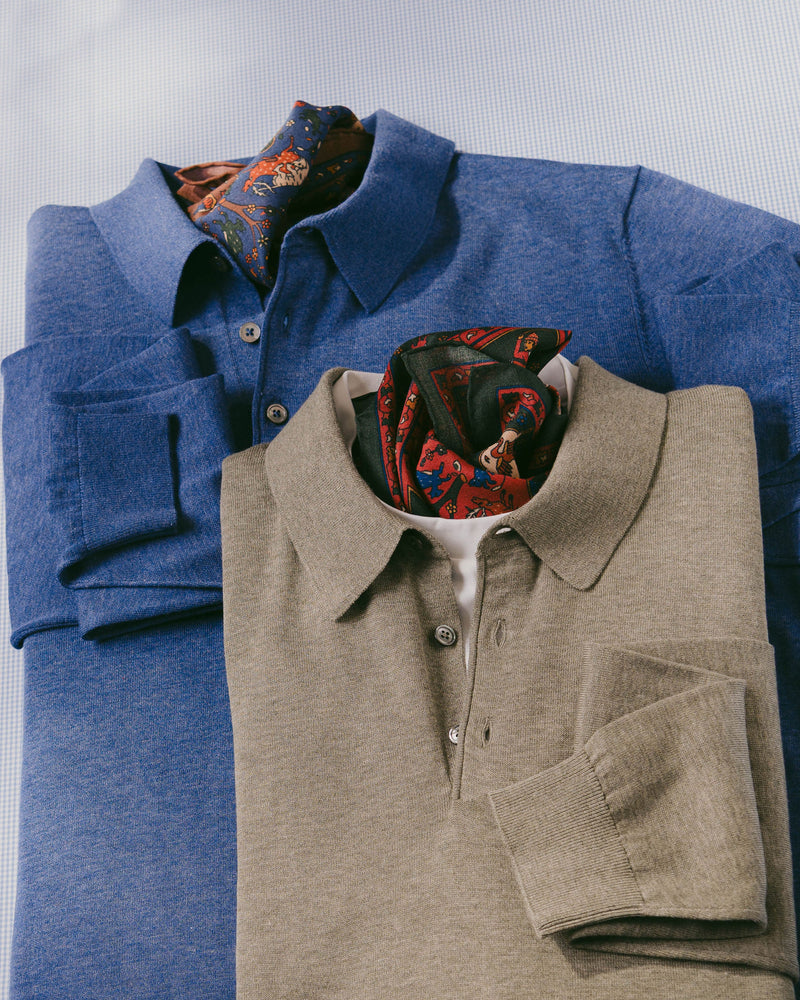 Two folded polo shirts, one blue and one beige, with a patterned pocket square on a light gray background.