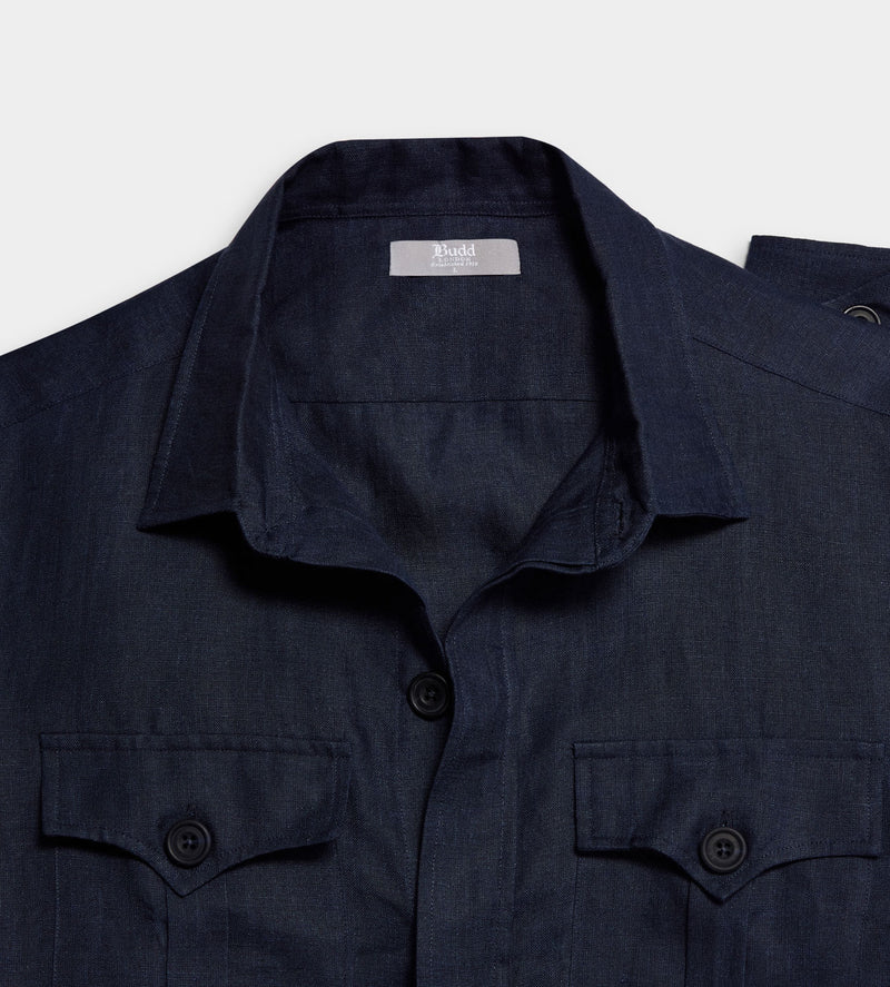 Close-up of a dark navy blue shirt jacket with a spread collar, button front, and two buttoned chest pockets on a light gray background.