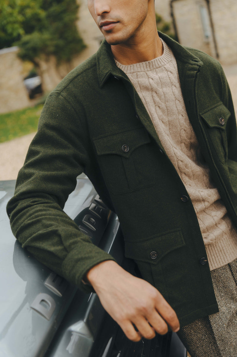 Man wearing a green coat over a beige sweater, standing next to a car.