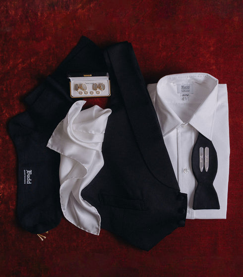 Dresswear accessories and black tie shirt laid out on red velvet background