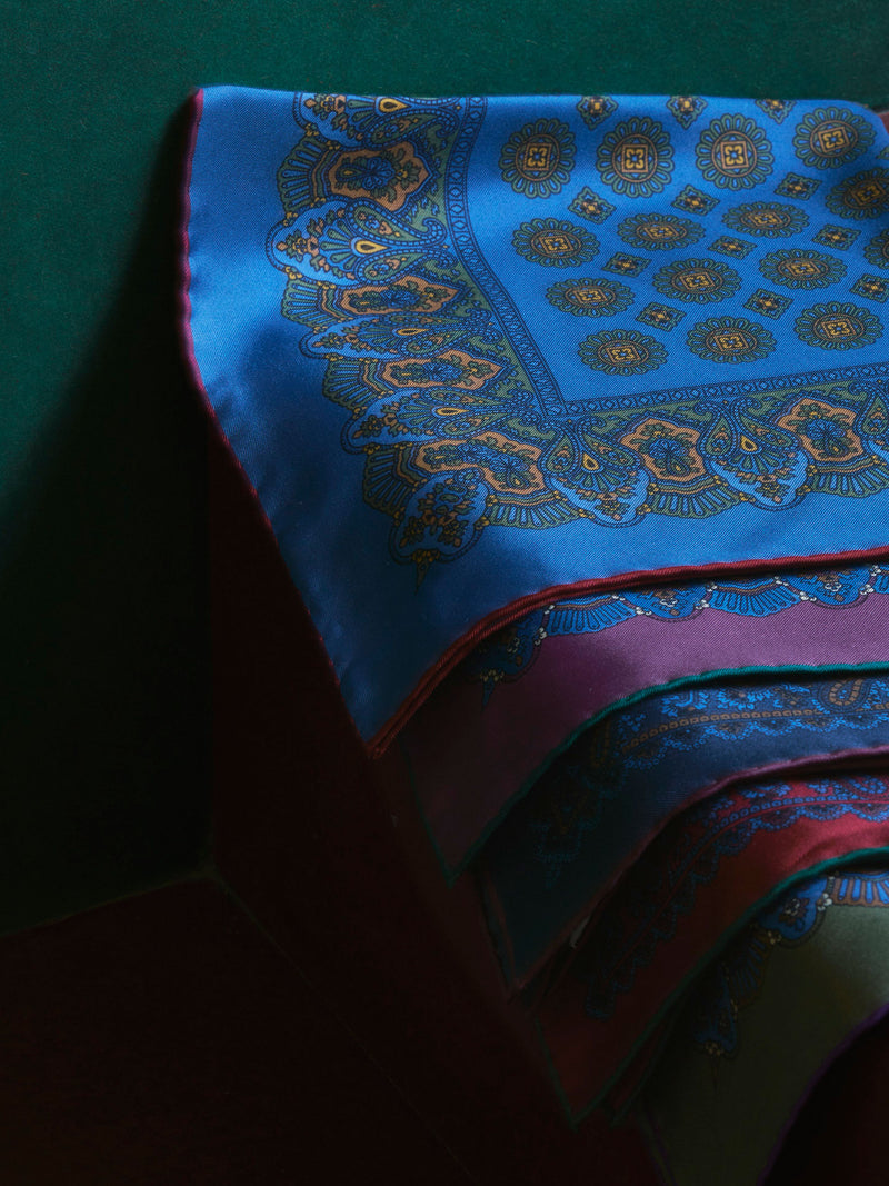 Silk pocket squares with an ornate pattern design in blue, burgundy, red and olive green against bottle green wall