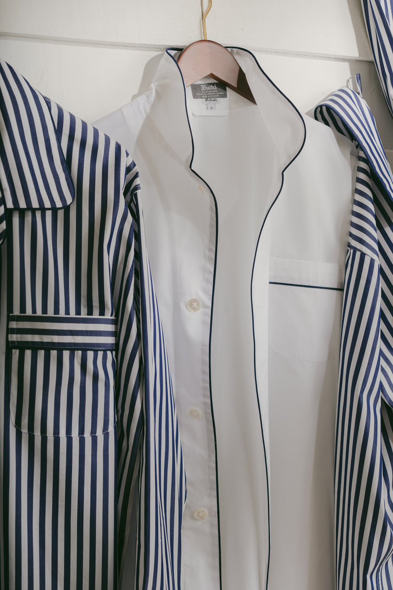 White pyjama shirt with black trim on a hanger next to striped pyjama shirts
