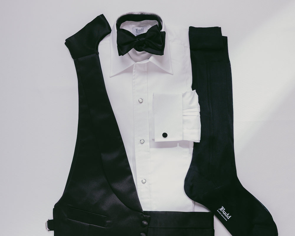 Black vest, white shirt with black bow tie, and black socks on a light gray background