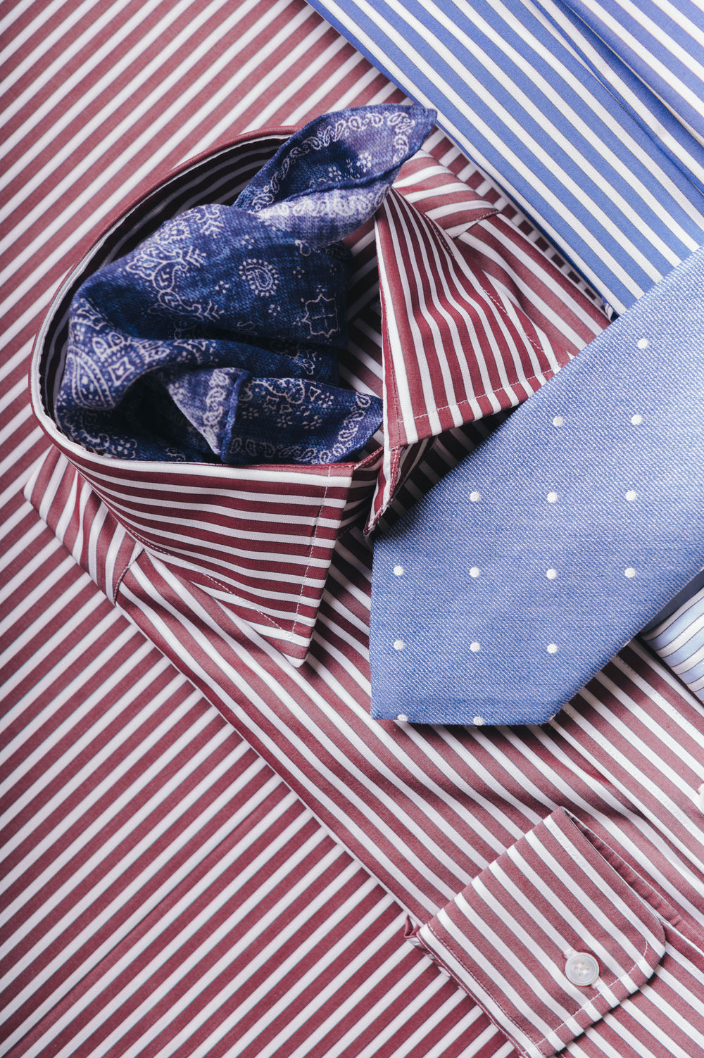 Red and white striped shirt with blue patterned pocket square and blue tie.