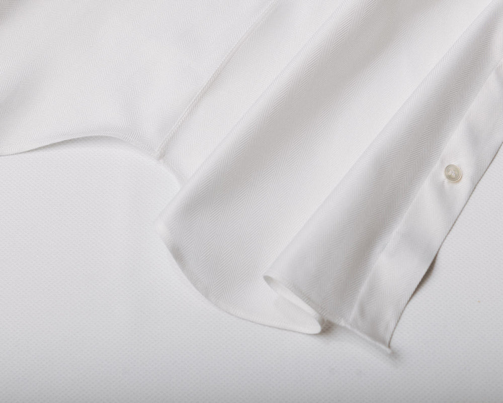 Close-up of a white long-sleeve button-up shirt showing the fabric texture, collar seam, and two buttons on the cuff.
