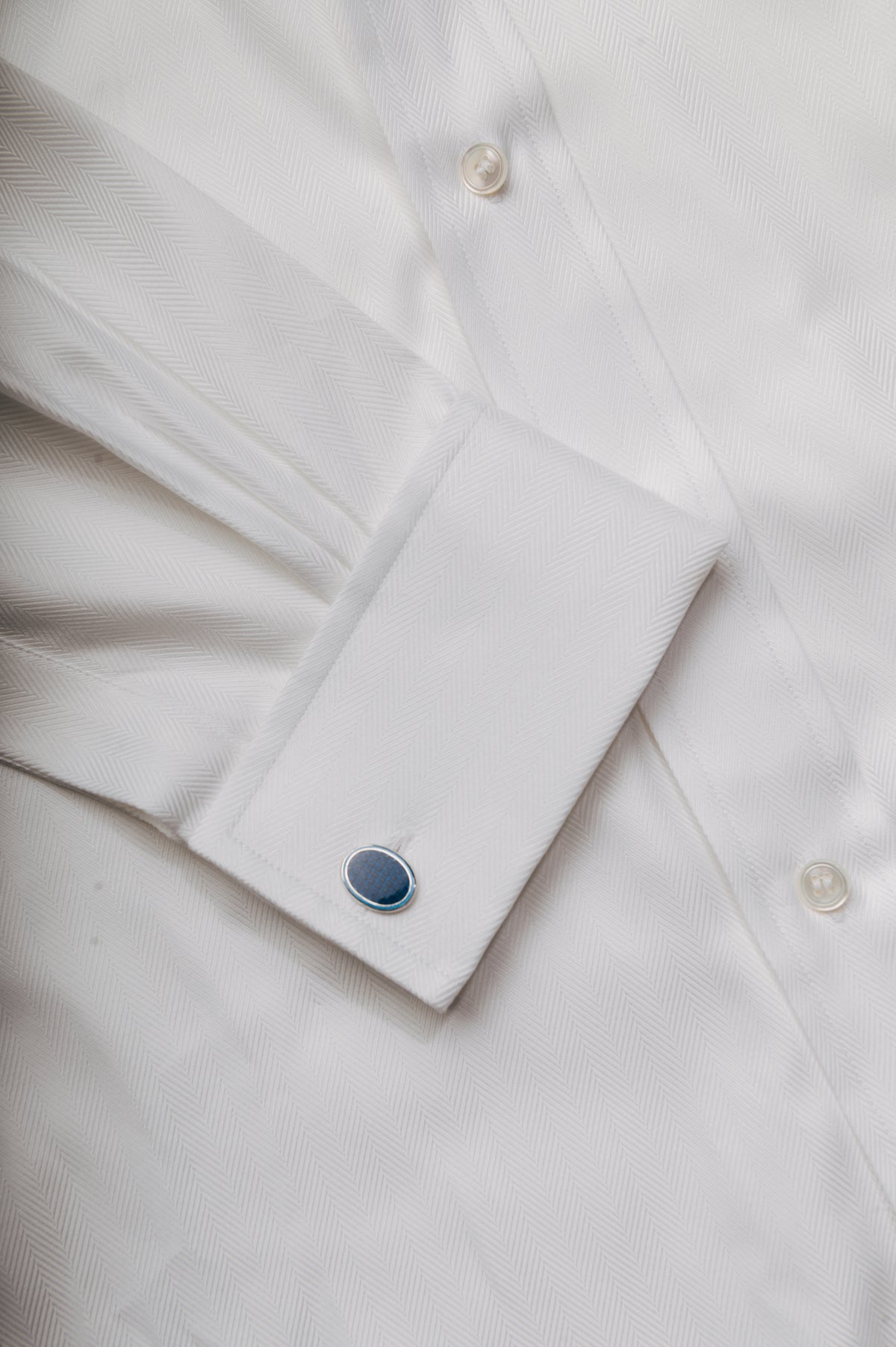 Close-up of a white dress shirt cuff with a single dark blue oval cufflink on a matching white shirt body.