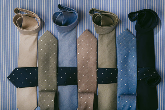 Selection of plain and spotted ties laid overlapping on blue stripe background