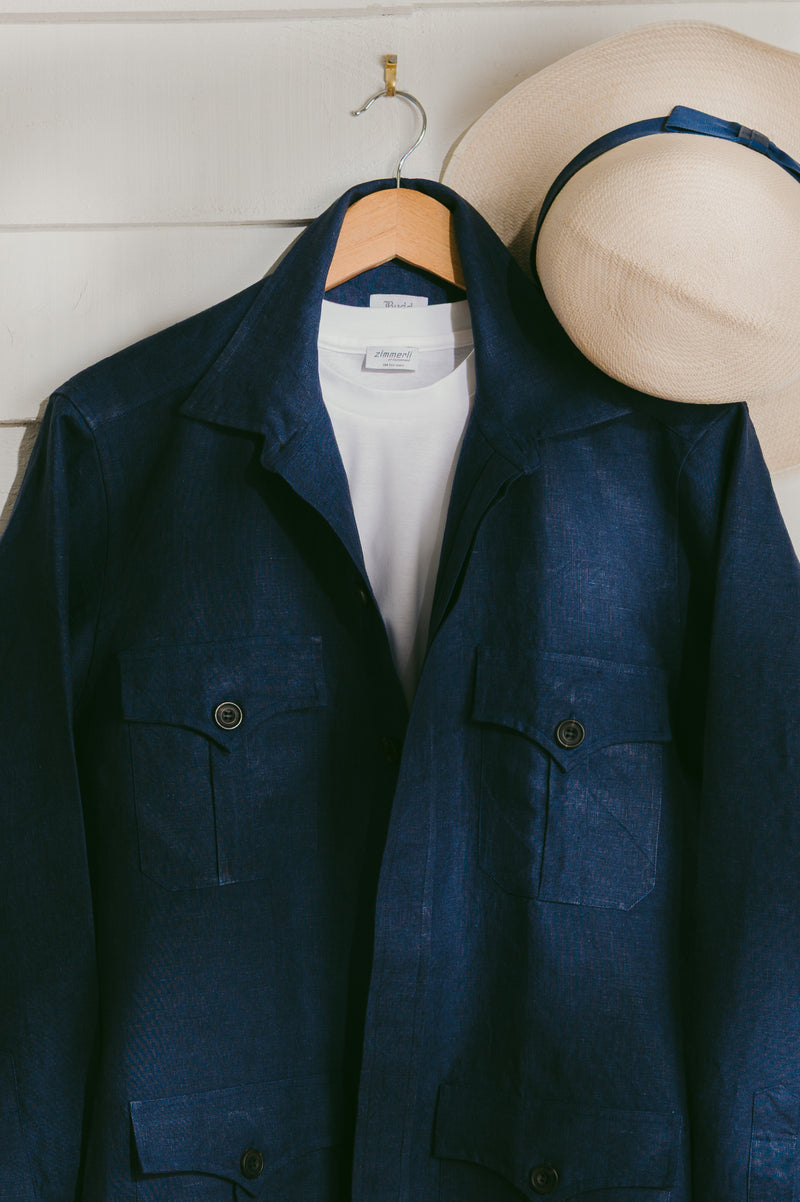 Navy blue jacket on a hanger with a white shirt underneath, next to a beige hat on a wooden surface.