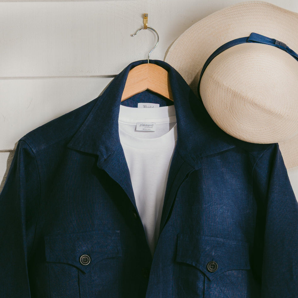 Navy blue jacket on a hanger with a white shirt underneath, next to a beige hat on a wooden surface.