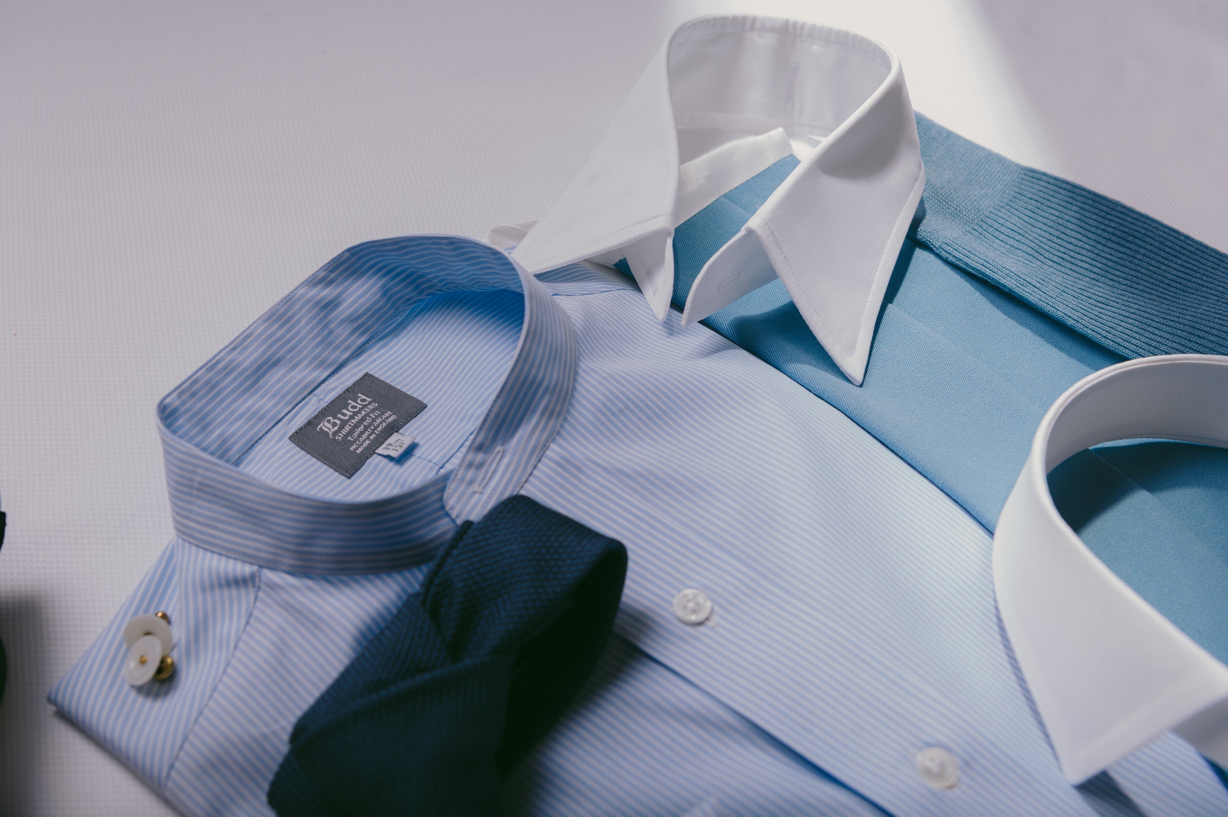 Light blue dress shirt with white collar and cuffs, black tie, and blue tie on a white background